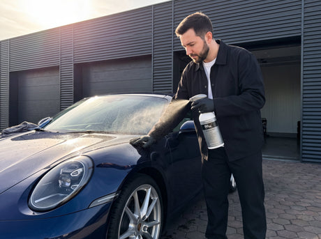 Daniel sprüht Koch-Chemie Spray Sealant S0.02 auf den Lack eines dunkelblauen Porsche 911 vor der Detailing1-Werkstatt
