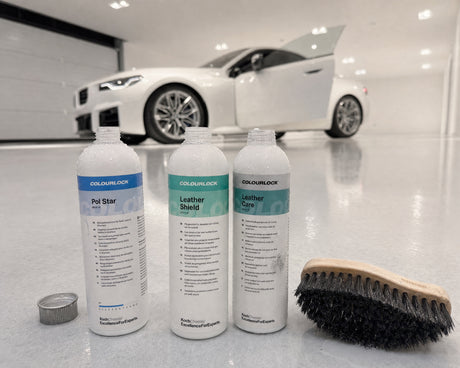 Detailing1 COLOURLOCK Pol Star, Leather Shield und Leather Care mit Lederbürste auf dem Hallenboden neben dem weißen BMW M2 —