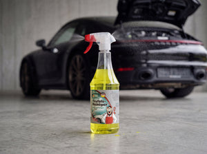 TUGA Chemie Teufels-Reiniger 1L Sprühflasche mit gelber Flüssigkeit und rotem Sprüh-Trigger auf Betonvorplatz vor schwarzem Porsche 911 mit offenem Heck